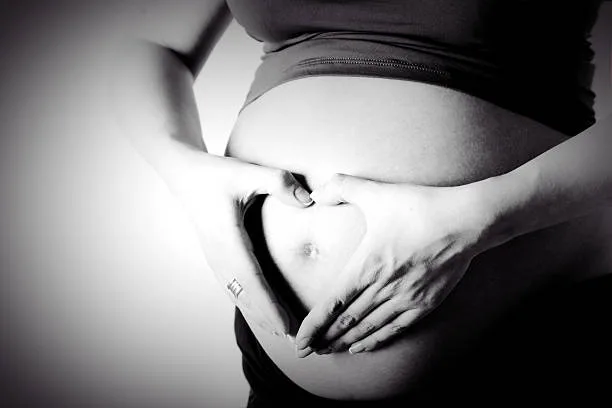 Future maman posant doucement ses mains sur son ventre, dans une lumière apaisante